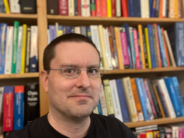 Headshot of Tony with a crowded bookshelf in the background